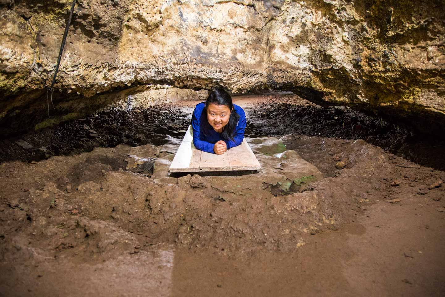 Julie crawling under a low rock in the lava tube, Santa Cruz Island, Galápagos Islands, Ecuador