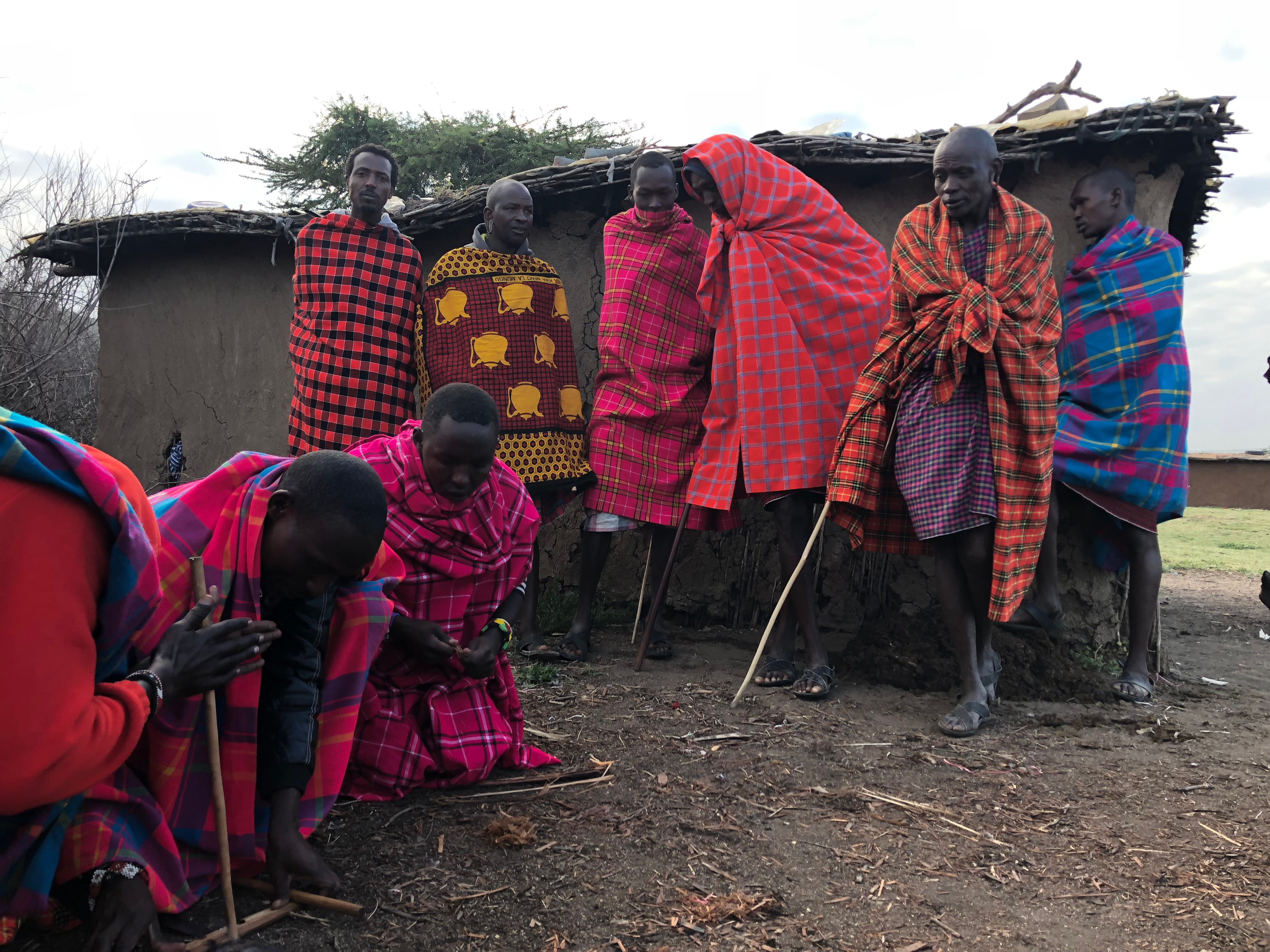 Maasai men starting a fire by hand by their houses.