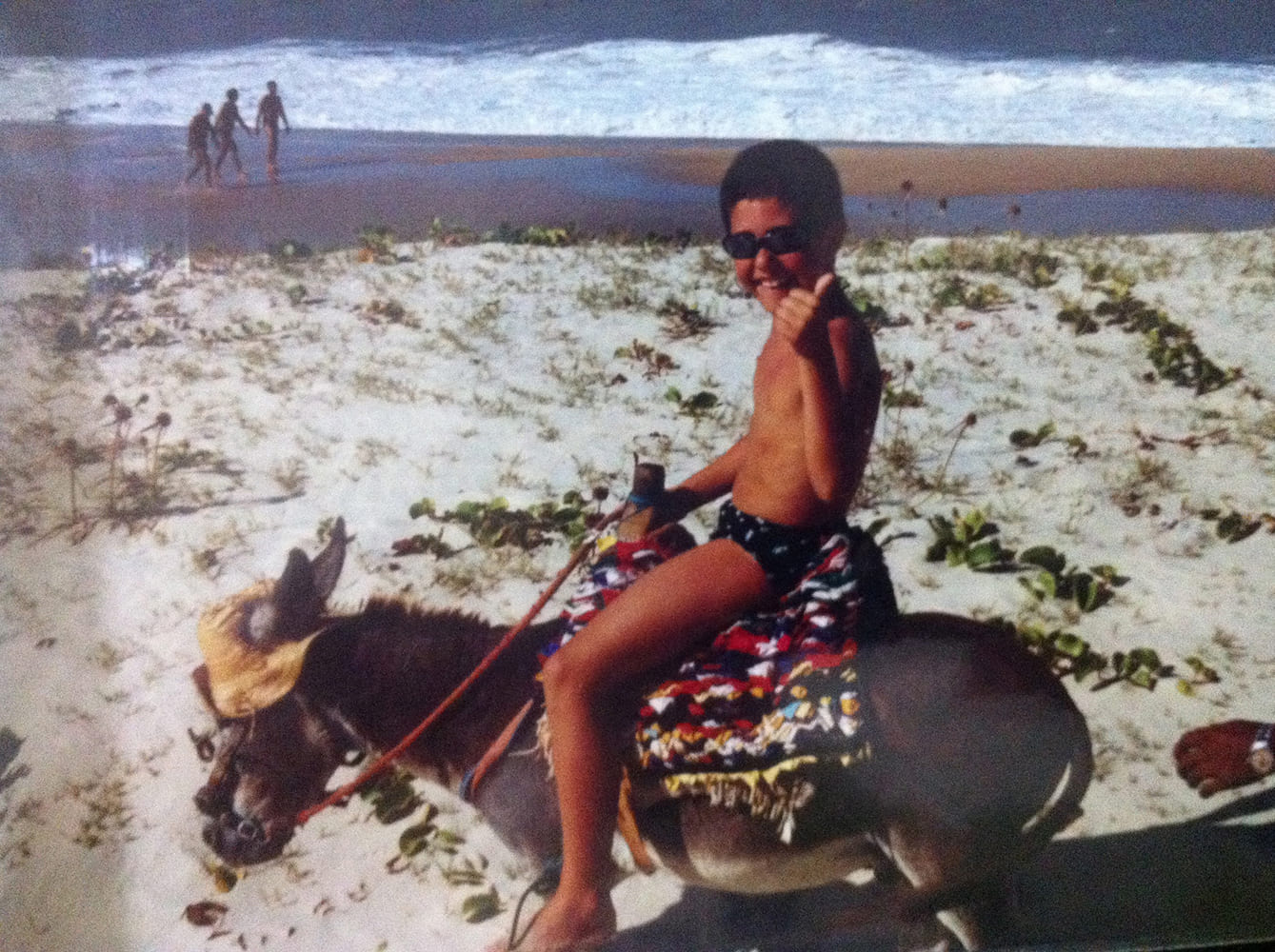 Young Carlos riding a donkey on the beach.